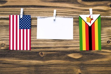 Wall Mural - Hanging flags of United States and Zimbabwe attached to rope with clothes pins with copy space on white note paper on wooden background.Diplomatic relations between countries.