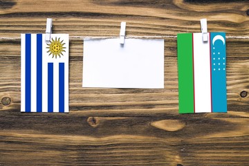 Wall Mural - Hanging flags of Uruguay and Uzbekistan attached to rope with clothes pins with copy space on white note paper on wooden background.Diplomatic relations between countries.