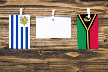Wall Mural - Hanging flags of Uruguay and Vanuatu attached to rope with clothes pins with copy space on white note paper on wooden background.Diplomatic relations between countries.