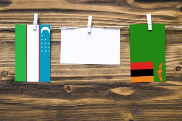 Wall Mural - Hanging flags of Uzbekistan and Zambia attached to rope with clothes pins with copy space on white note paper on wooden background.Diplomatic relations between countries.