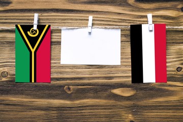 Wall Mural - Hanging flags of Vanuatu and Yemen attached to rope with clothes pins with copy space on white note paper on wooden background.Diplomatic relations between countries.