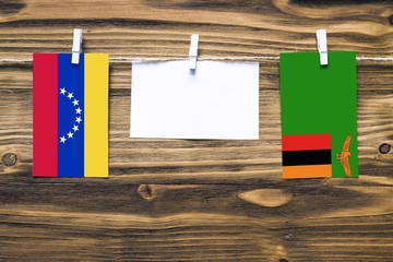Wall Mural - Hanging flags of Venezuela and Zambia attached to rope with clothes pins with copy space on white note paper on wooden background.Diplomatic relations between countries.