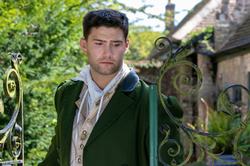 Portrait of handsome gentleman dressed in vintage costume standing next to iron gate, looking pensive