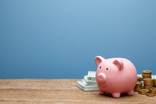Pink Piggy Bank And Money With Banknotes And Coins On A Wooden Table And Blue Background. Copy Space For Text.
