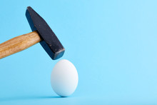 A Hammer Is About To Crush And Egg Shell On Blue Background