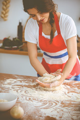 Young brunette woman cooking pizza or handmade pasta in the kitchen. Housewife preparing dough on wooden table. Dieting, food and health concept