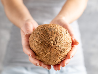 Girl in gray t-shirt and blue jeans holding coconut in hand on gray background