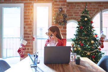 Sticker - Beautiful woman sitting at the table working with laptop at home around christmas tree covering eyes with hands and doing stop gesture with sad and fear expression. Embarrassed and negative concept.