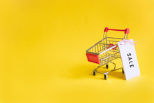 Toy Supermarket Cart With Sale Sticker On A Yellow Background. Concept Sales, Shopping And Black Friday. Copyspace For Text.