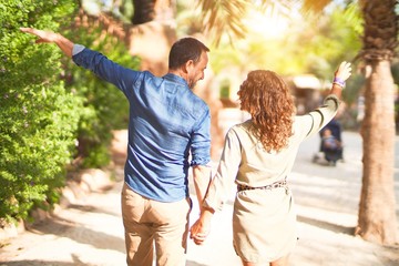 Middle age beautiful couple smiling happy and confident at town park. Walking with smile on face on backview