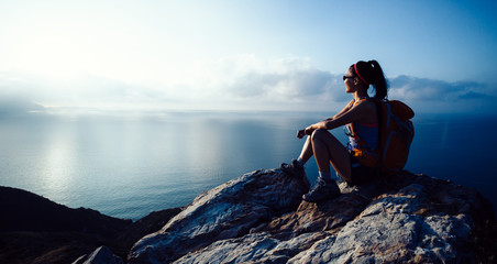 Wall Mural - Young woman hiker enjoy the view at sunrise seaside mountain peak