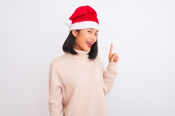 Young beautiful chinese woman wearing Christmas Santa hat over isolated white background pointing finger up with successful idea. Exited and happy. Number one.