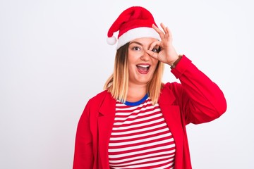 Canvas Print - Young beautiful woman wearing Christmas Santa hat over isolated white background doing ok gesture with hand smiling, eye looking through fingers with happy face.