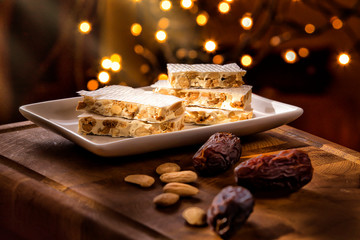 Christmas Concept. Alicante nougat in the foreground, in a warm home atmosphere at Christmas. There are Christmas lights in the background.