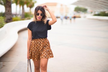 Young beautiful girl wearing sunglasses, t-shirt and animal print skirt walking at the park