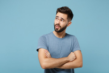 Young pensive handsome man in casual clothes posing isolated on blue background, studio portrait. People sincere emotions lifestyle concept. Mock up copy space. Holding hands crossed, looking aside.