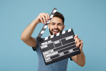 Sticker - Young cheerful man in casual clothes posing isolated on blue wall background, studio portrait. People lifestyle concept. Mock up copy space. Holding in hands classic black film making clapperboard.