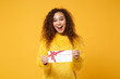 Excited young african american girl in fur sweater posing isolated on yellow orange background studio portrait. People lifestyle concept. Mock up copy space. Hold gift certificate, keeping mouth open.