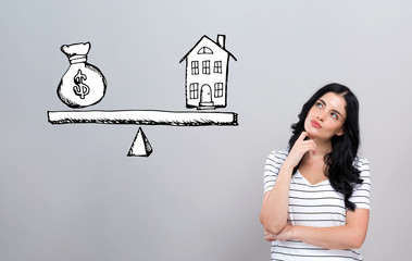 Wall Mural - House and money on the scale with young woman in a thoughtful face