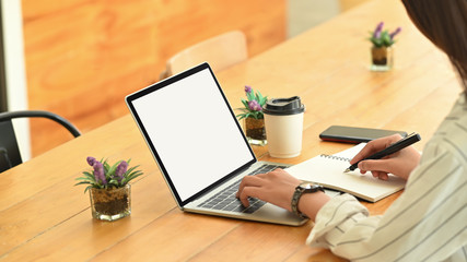 Cropped shot female using isolated screen laptop and writing notebook.