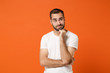 © ViDi Studio - Confused pensive young man in casual white t-shirt posing isolated on orange background, studio portrait. People sincere emotions lifestyle concept. Mock up copy space. Putting hand prop up on chin.