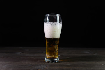 Photo of beer in a glass. Thick foam and a nice color drink on a black background.