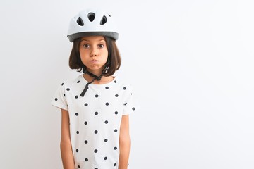 Poster - Beautiful child girl wearing security bike helmet standing over isolated white background puffing cheeks with funny face. Mouth inflated with air, crazy expression.