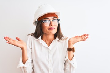 Poster - Young beautiful architect woman wearing helmet and glasses over isolated white background clueless and confused expression with arms and hands raised. Doubt concept.