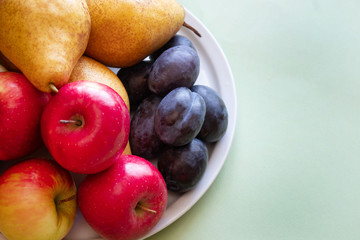 Fresh organic pears, apples, plums on an orange background. Autumn harvest. Free space for text.