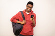 © mimagephotos - smiling young african american man with glasses and bag holding mobile phone by white background