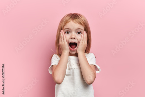 Photographie Close up photo little beautiful emotioal excited girl touching her cheeks, close