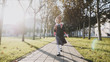 © alexeg84 - Young blonde girl with a pink backpack in school uniform is walking quickly in the park on path at sunny autumn weather, looking around and smiling. Trees along the way, front view.