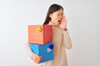 © Krakenimages.com - Young chinese woman holding birthday gifts over isolated white background shouting and screaming loud to side with hand on mouth. Communication concept.