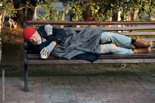 Fotomural Vagrant male lying on street bench asking for money, for any help