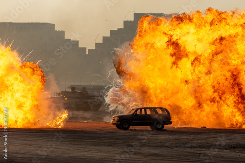 Cuadros en Lienzo Close up of a Military strike or strike or bomb in war on an SUV with tanks causing fire balls and explosion in the town in chaos