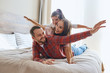 © alfa27 - Joyful playful family resting on big wide bed in brightly lighted hotel room, playing with cheerful expression, having fun, enjoying holidays, stretching hands, looking away, expressing happiness