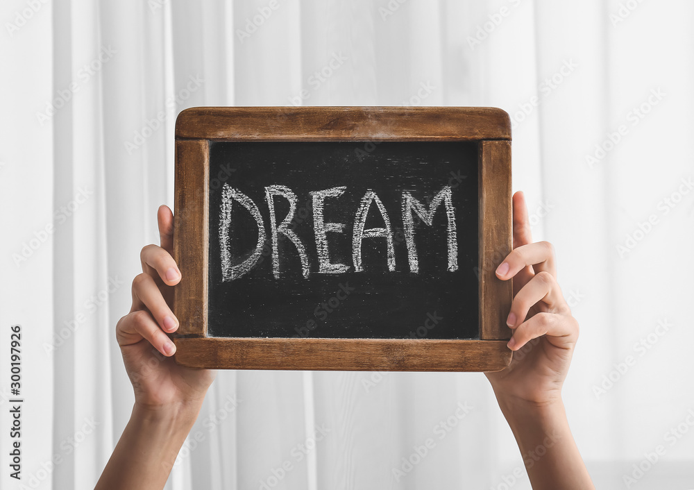 Female hands with word DREAM written on chalkboard