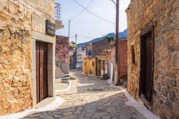 Narrow street with colorful stone houses in the old village of Pano Elounda, Crete, Greece. 