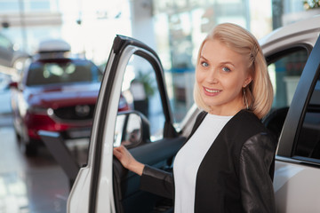 Wall Mural - Lovely happy woman smiling joyfully, buying new car at the dealership, copy space