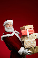 Waist Up Portrait Of Fairytale Santa Holding Stack Of Christmas Presents Over Red Background, Copy Space