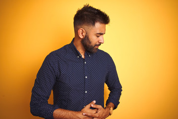 Wall Mural - Young handsome indian businessman wearing shirt over isolated yellow background with hand on stomach because nausea, painful disease feeling unwell. Ache concept.