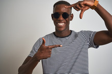 African American Man Wearing Striped T-shirt And Sunglasses Over Isolated White Background Smiling Making Frame With Hands And Fingers With Happy Face. Creativity And Photography Concept.