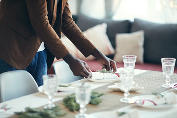 Cropped portrait of young African-American man preparing table setting while decorating dining room for Christmas party at home, copy space