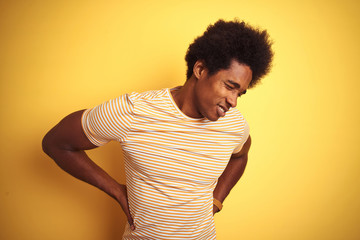 Poster - American man with afro hair wearing striped t-shirt standing over isolated yellow background Suffering of backache, touching back with hand, muscular pain