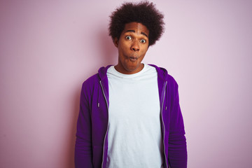 Poster - Young african american man wearing purple sweatshirt standing over isolated pink background making fish face with lips, crazy and comical gesture. Funny expression.