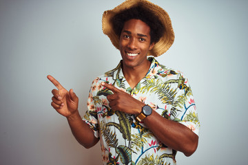 Sticker - Afro american man on vacation wearing summer shirt and hat over isolated white background smiling and looking at the camera pointing with two hands and fingers to the side.