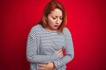 Sticker - Young redhead woman wearing strapes navy shirt standing over red isolated background with hand on stomach because nausea, painful disease feeling unwell. Ache concept.