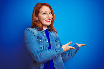 Sticker - Young beautiful redhead woman wearing denim shirt standing over blue isolated background Inviting to enter smiling natural with open hand