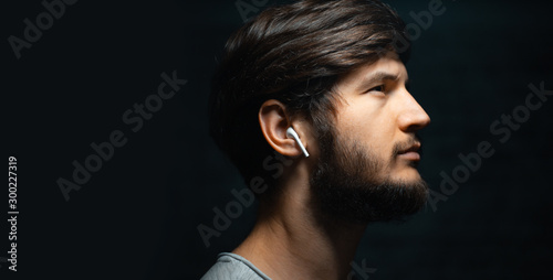 Fotomural Close-up portrait of young man with wireless earphones, on black background