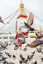 Beautiful Female Sincerely Smiling And Going By Square Through Pigeons Flock With Boudhanath Stupa - The Largest Spherical Stupas In Nepal. Traveling Around The World Concept Image.